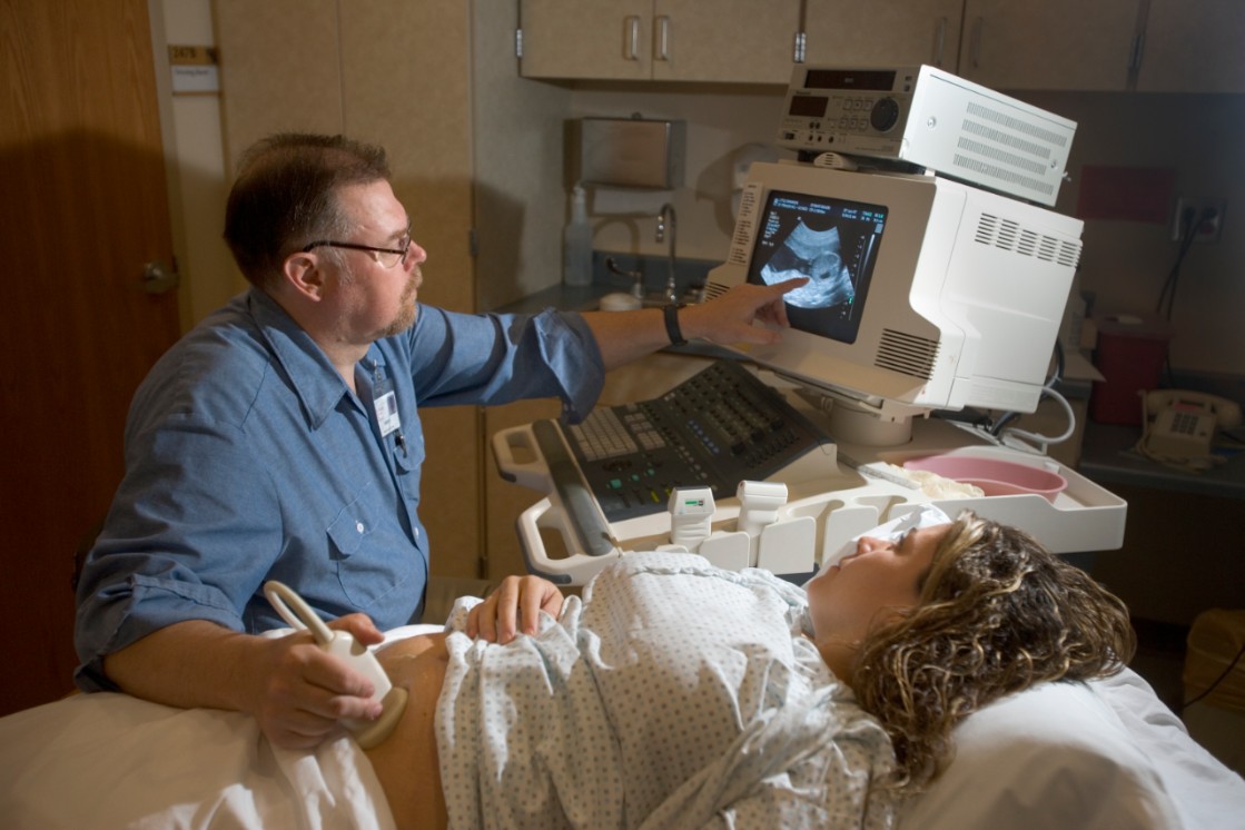 Patient getting an ultrasound test done by an ultrasound technician who is scanning her abdomen and pointing at the ultrasound image on a computer screen 